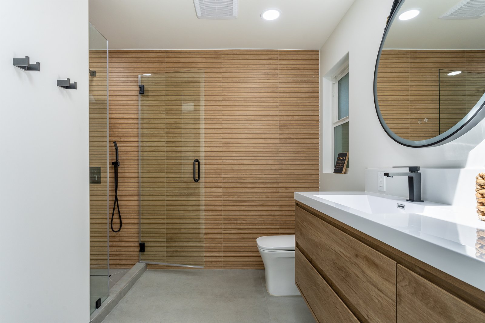 Contemporary bathroom remodel in Los Altos, CA, featuring a sleek glass shower, warm wood-paneled walls, floating vanity with wood finish, and modern fixtures for a clean, sophisticated design.