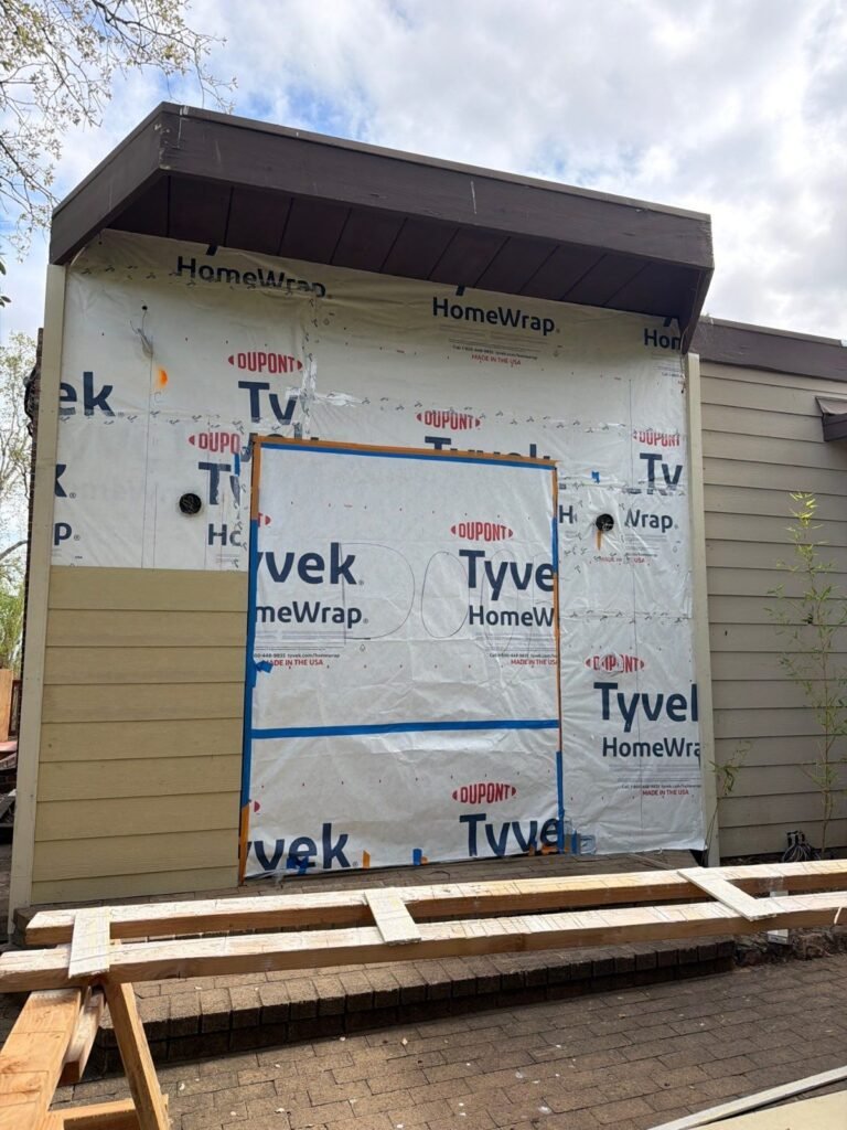 House wrap weather barrier with taped seams around a framed opening before siding