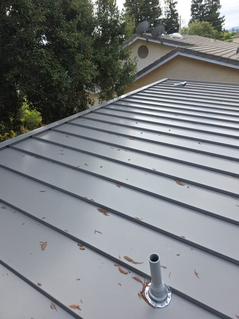Pipe vent boot flashing on a standing-seam metal roof, with pine needles to clear before winter rains
